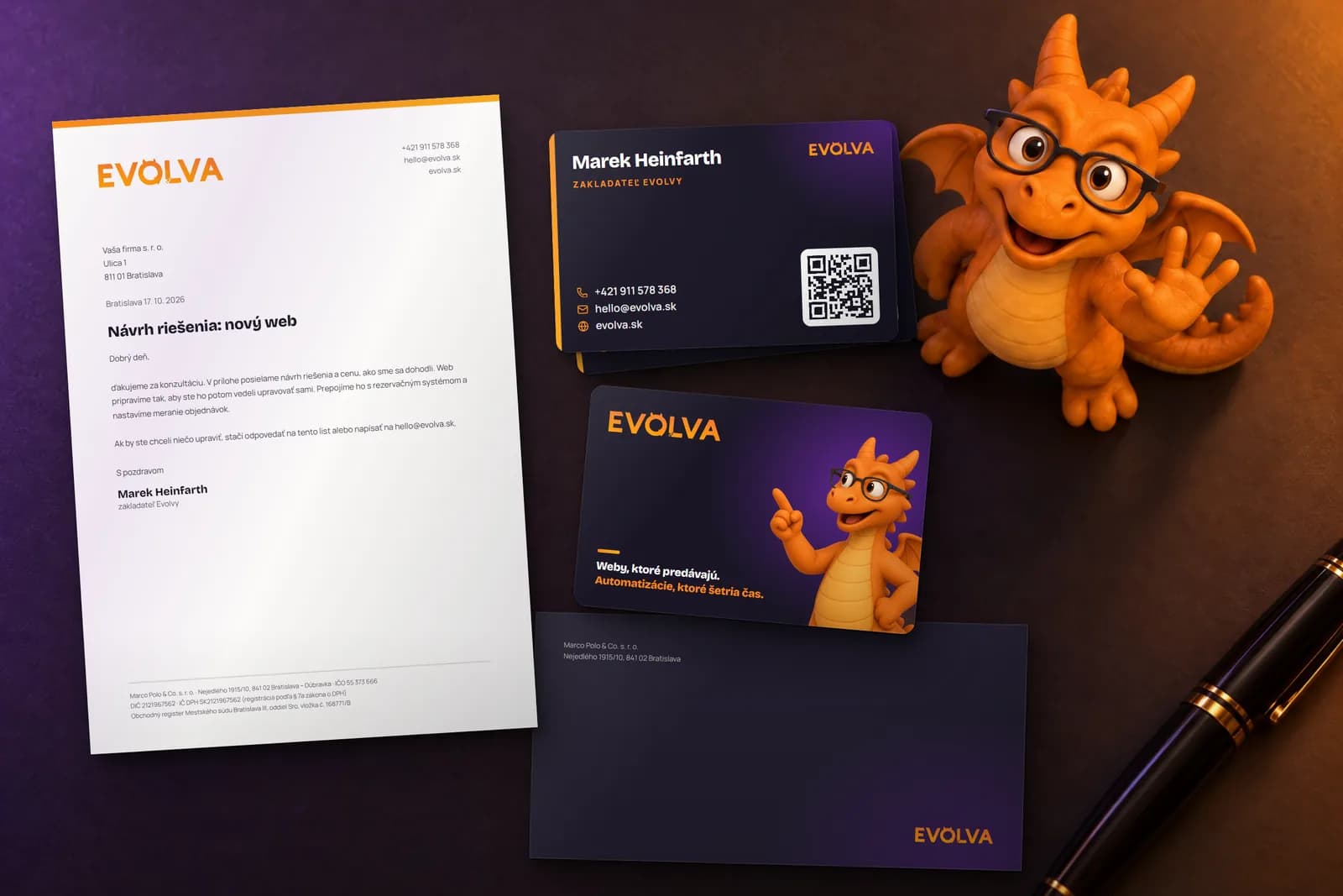 Tlačoviny Evolvy na tmavom stole: hlavičkový papier, vizitky z prednej aj zadnej strany a tmavá obálka, vedľa nich mávajúca figúrka dráčika